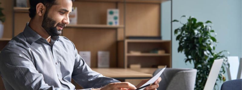 man sat at desk, reading CV with laptop infront. Featured on XCL Group website